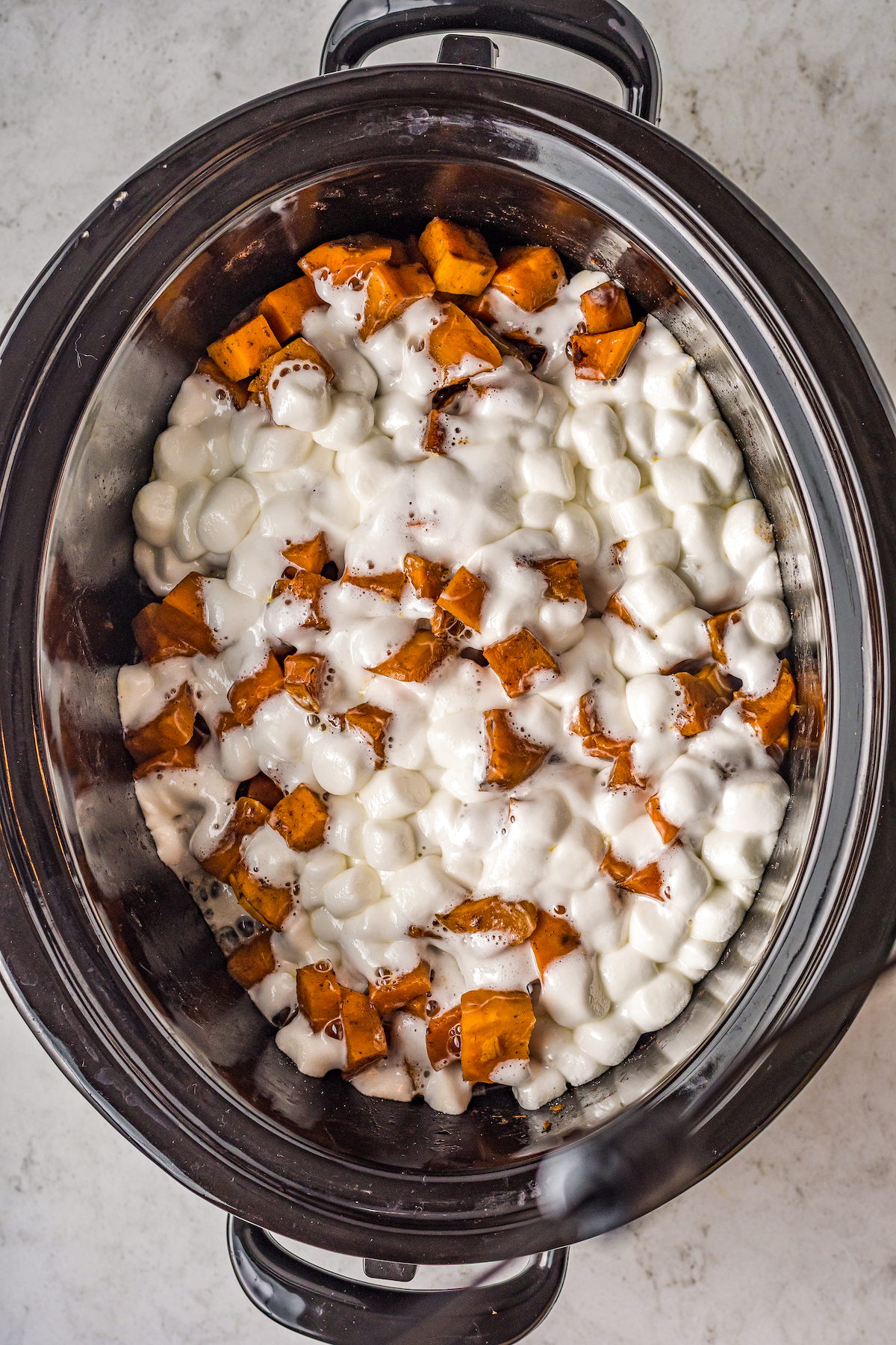 Sweet potatoes with marshmallows melted on top in a crockpot.
