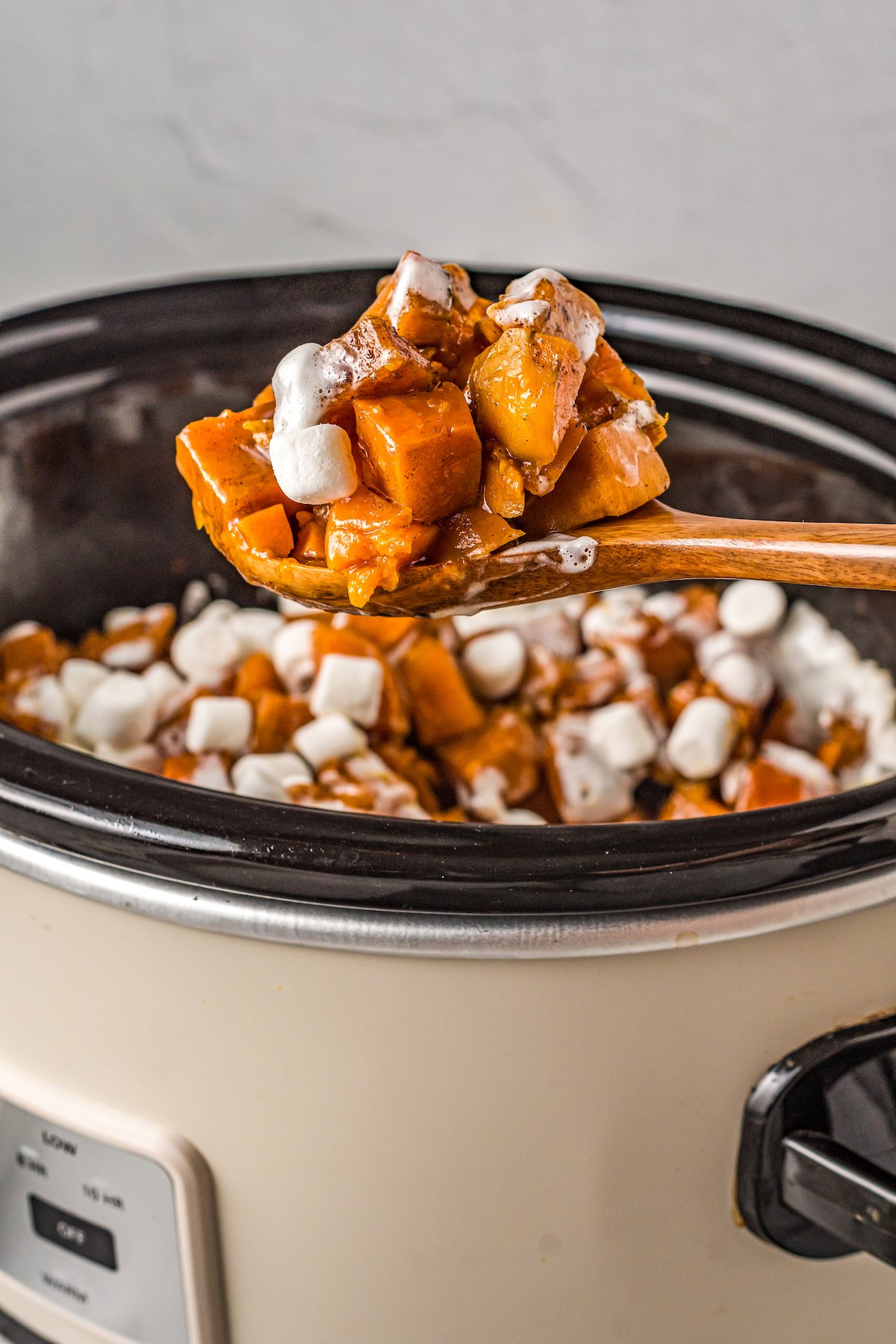 A wooden spoon scooping up a serving of crockpot sweet potatoes with marshmallows.