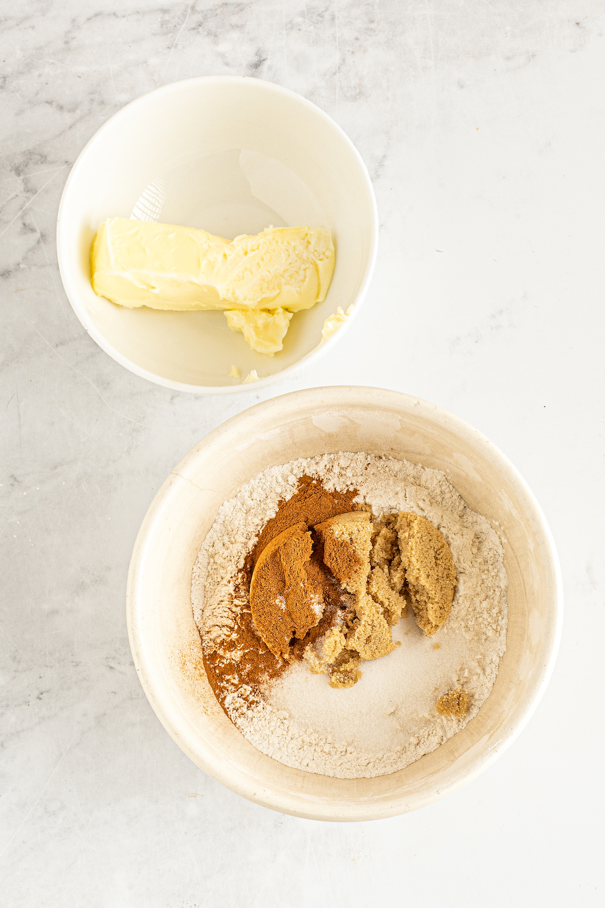 A bowl with butter next to a bowl with flour, brown sugar, and cinnamon