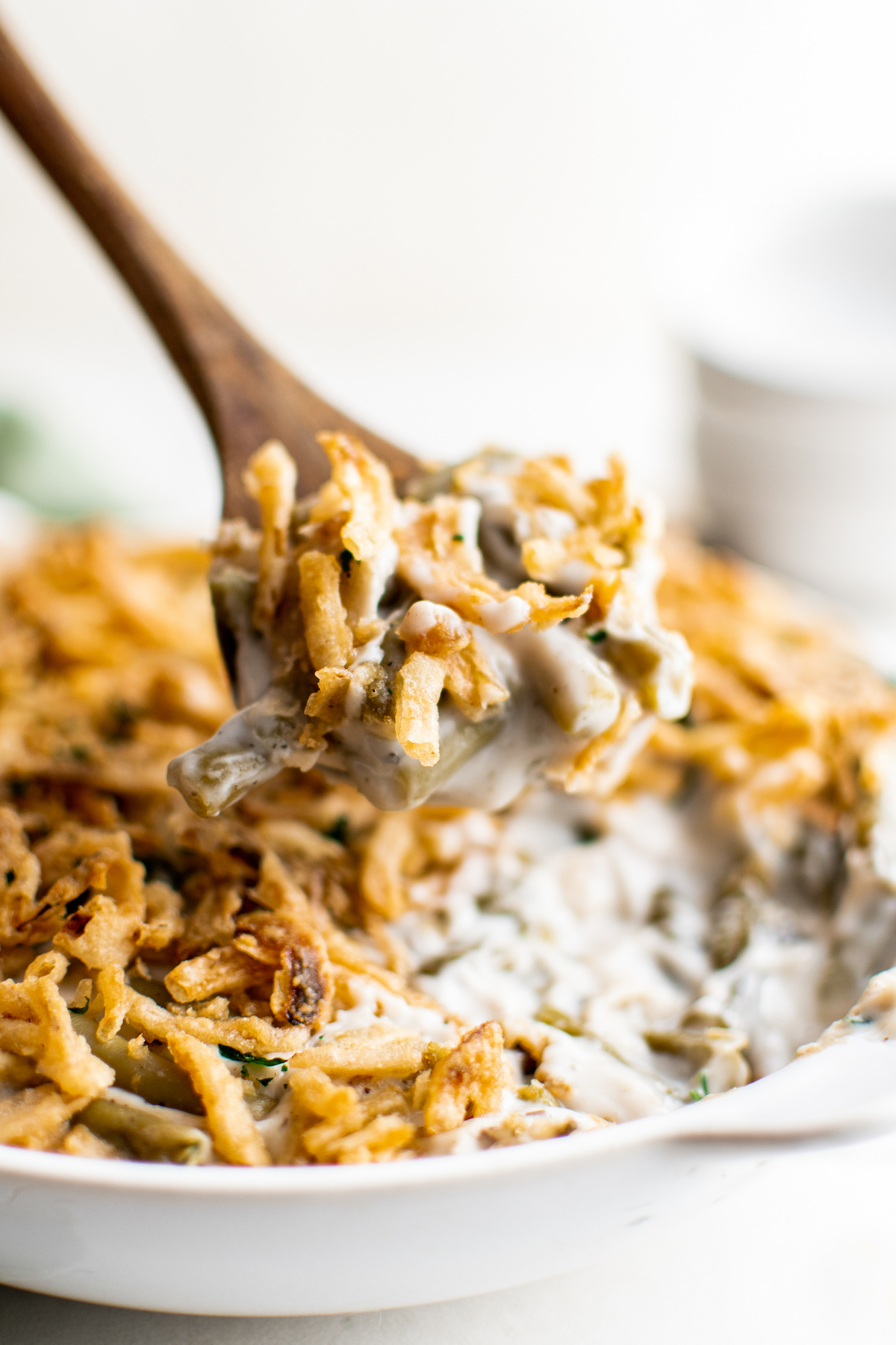 A wooden spoon lifting a portion of easy green bean casserole out of a dish.