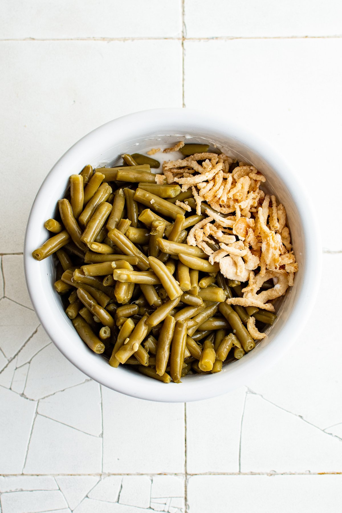 Green beans and fried onions in a mixing bowl with mushroom sauce.