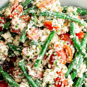 Green bean salad on a white plate with feta cheese and tomatoes.