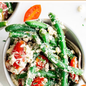 A bowl with green beans, tomatoes and feta with two forks.