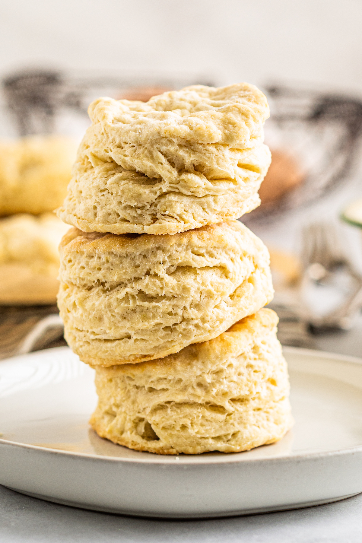 Three tall, flaky homemade biscuits stacked on top of each other.