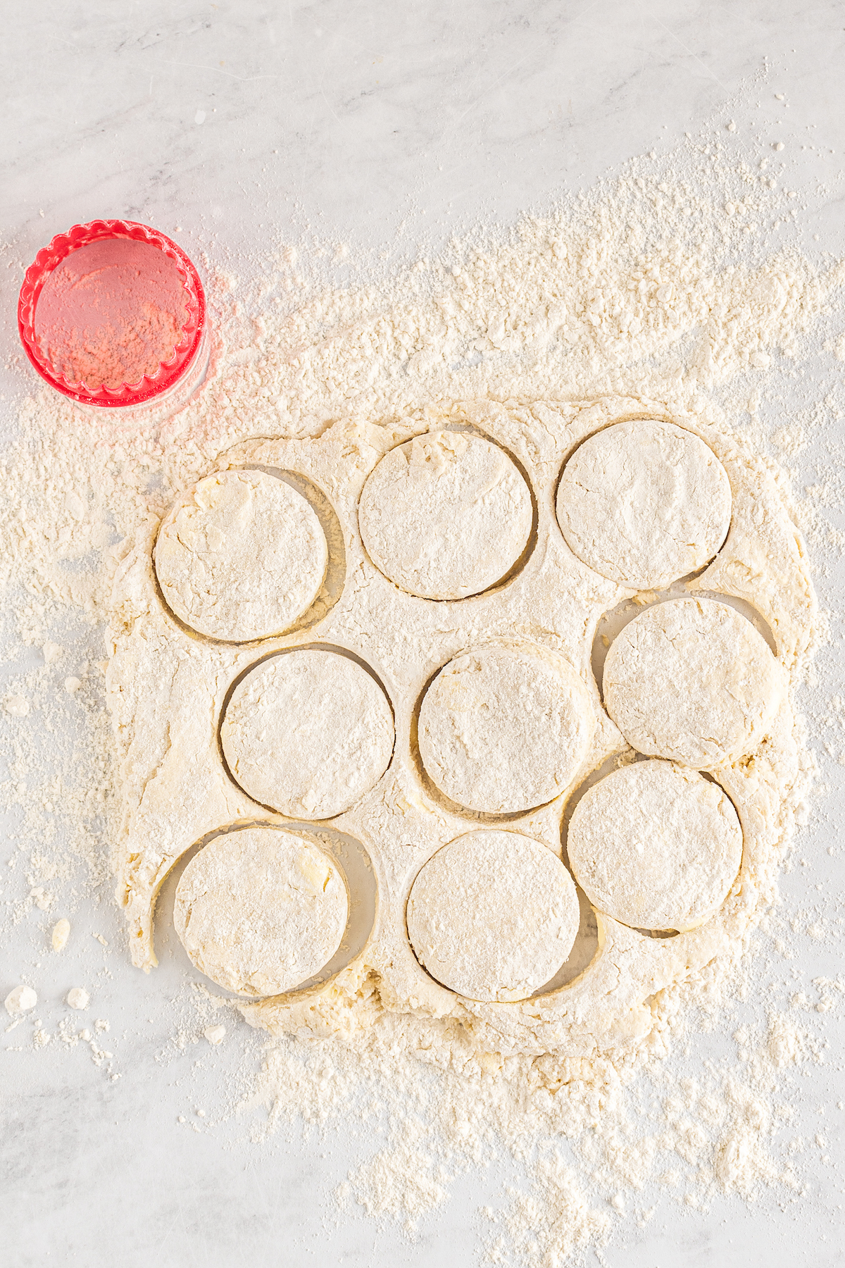 An uneven rectangle of dough on a floured work surface, with round biscuits cut out.