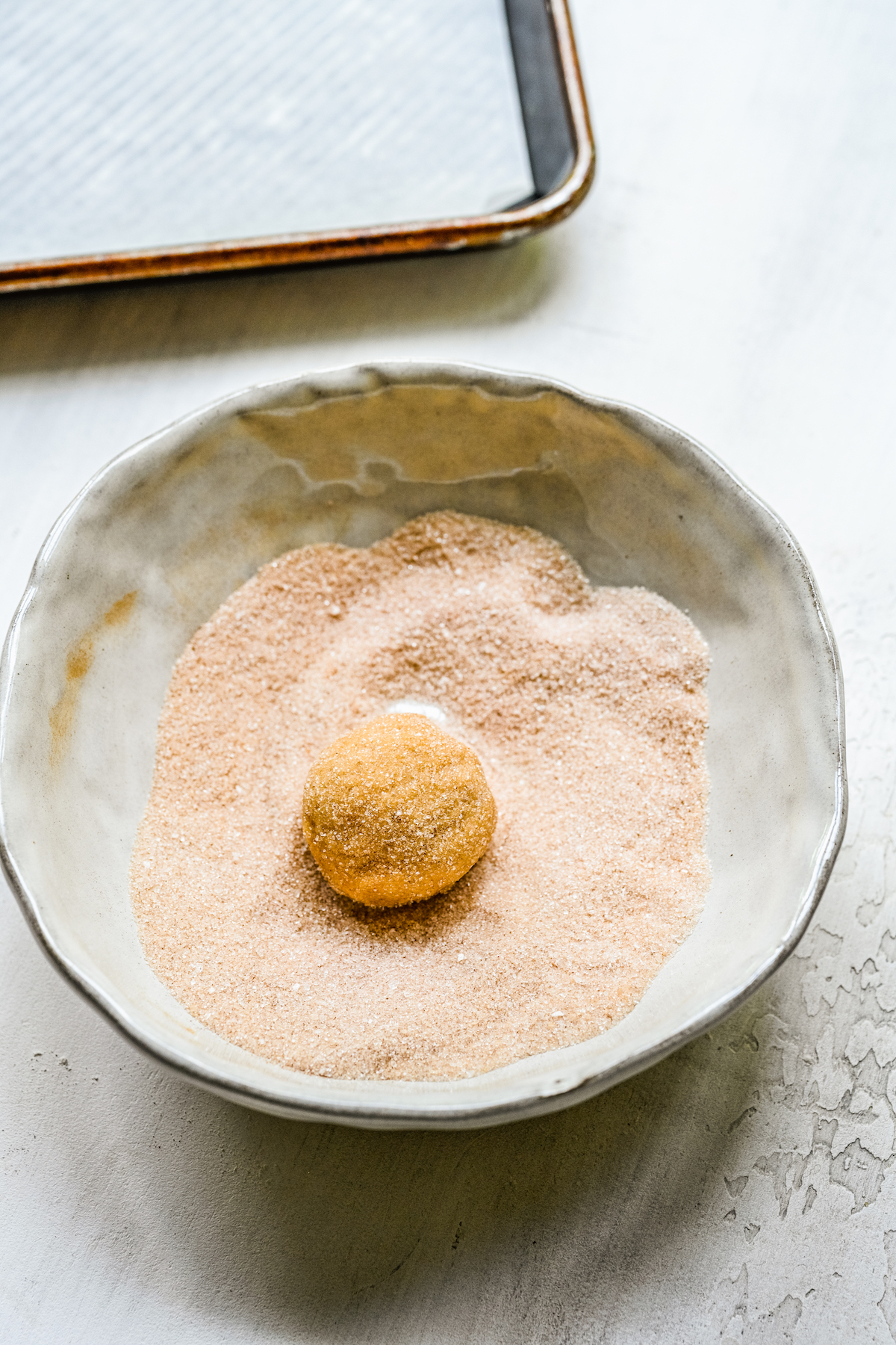 A ball of golden-brown cookie dough in a dish of cinnamon sugar.