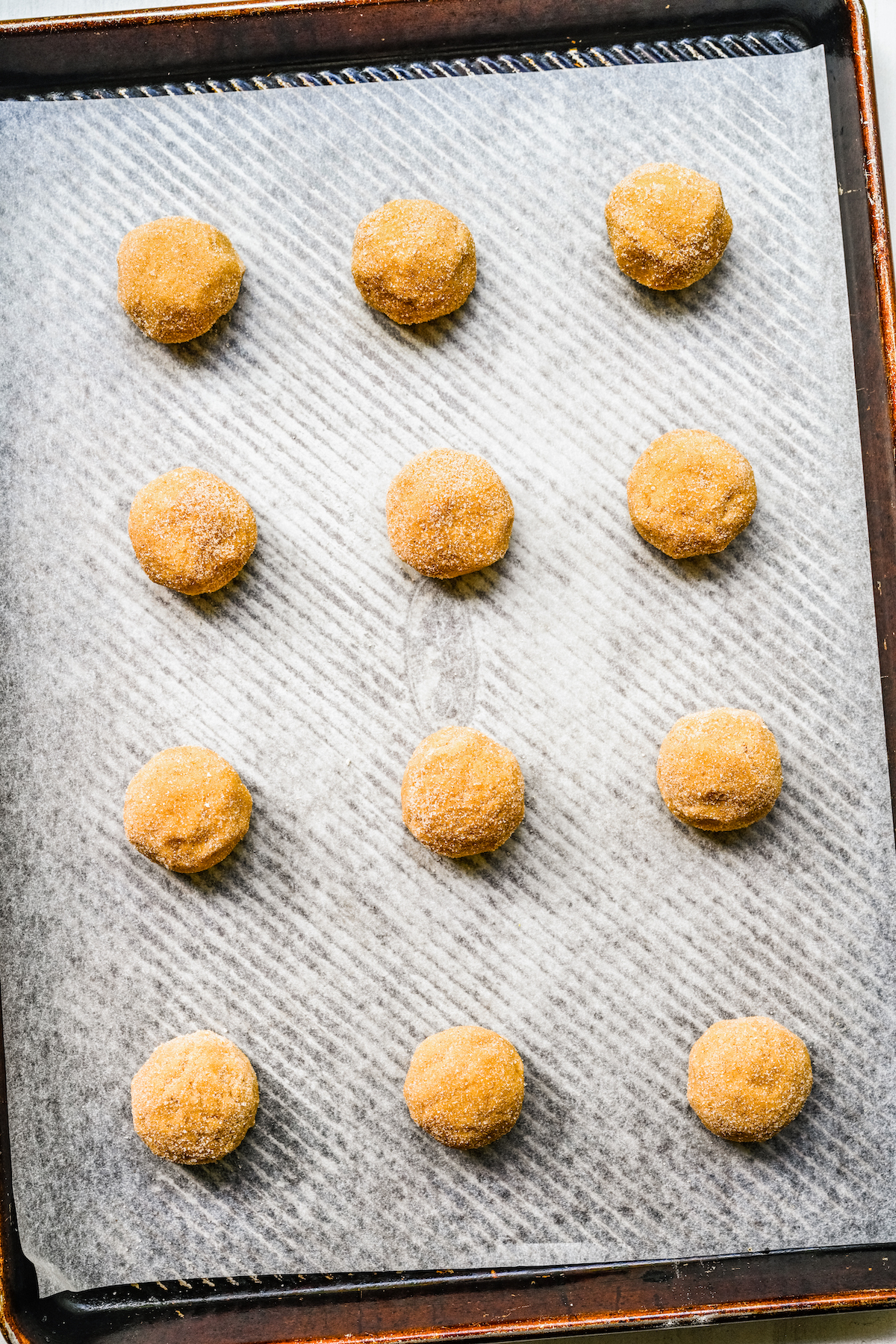 Cinnamon-sugar coated cookie dough balls, lined up on a baking sheet.