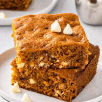 Two pumpkin bars stacked on a white plate, with white chocolate chips sprinkled over.