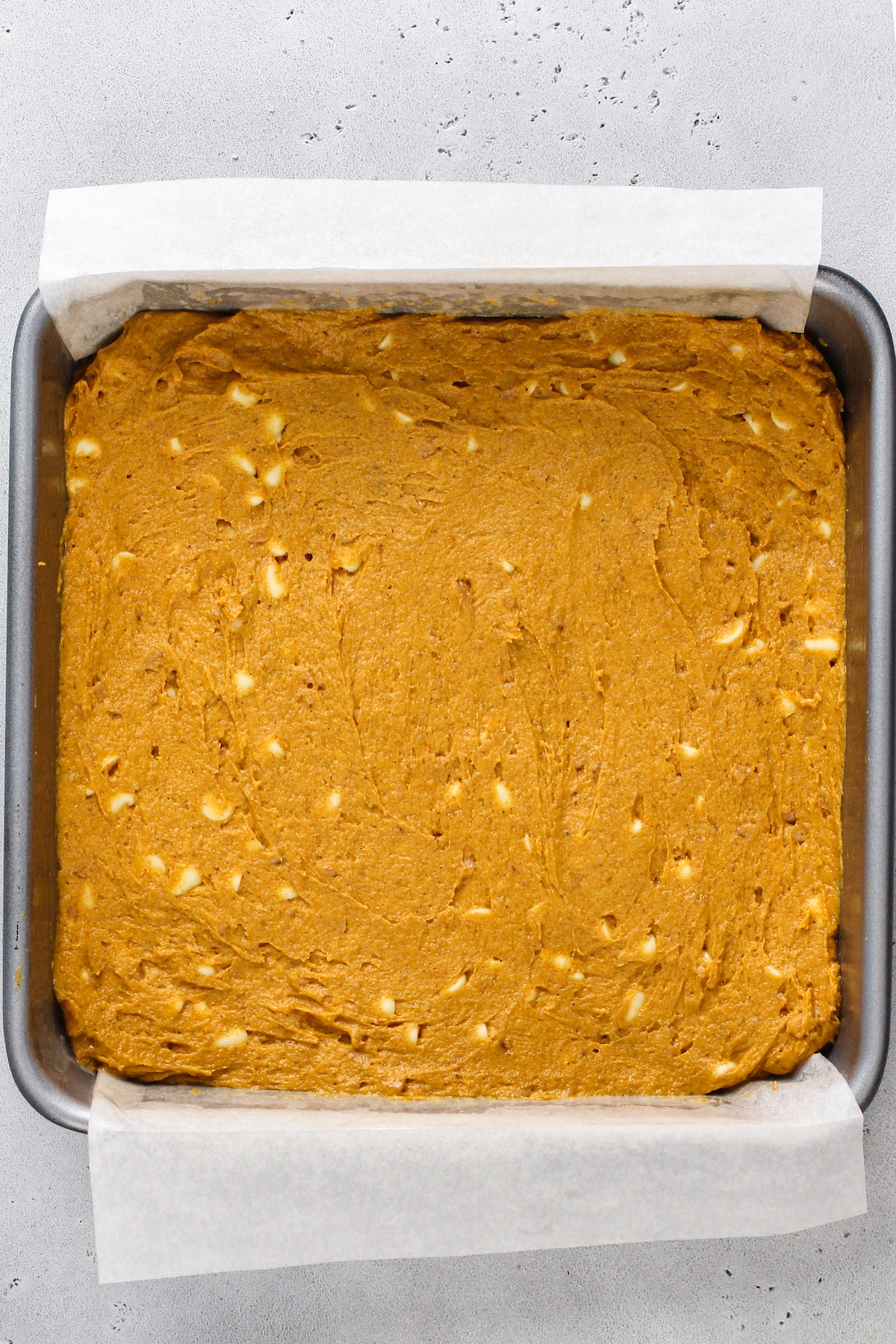 A square baking pan lined with parchment, and filled with pumpkin batter.
