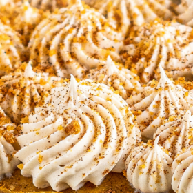 Pumpkin cheesecake with cream cheese pipped on top with crushed gingersnaps on top.