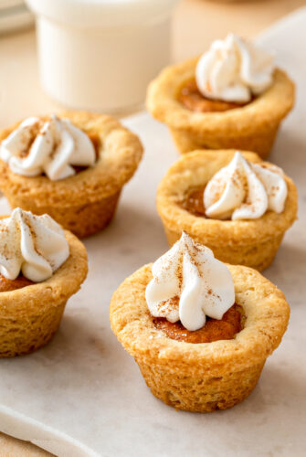 Mini pumpkin cookie cups garnished with whipped cream and pumpkin pie spice.