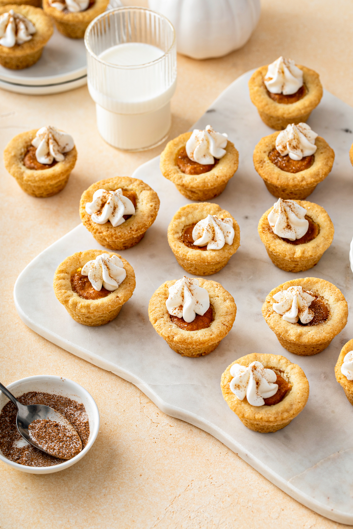 Mini pumpkin pie cookies on a cutting board with milk and pumpkin pie spice.