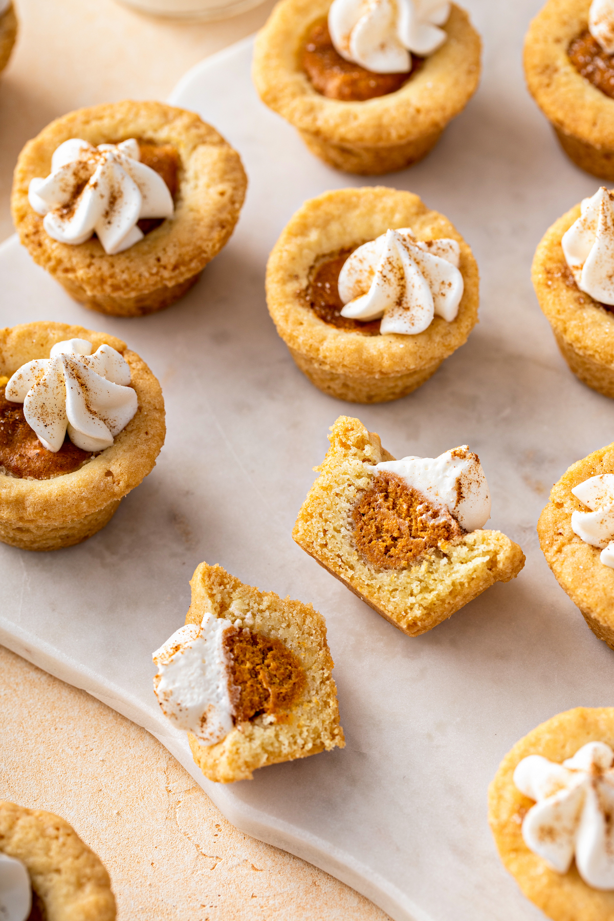 Several pumpkin pie cookies on a white cutting board, with one of the cookies cut in half to show the texture.