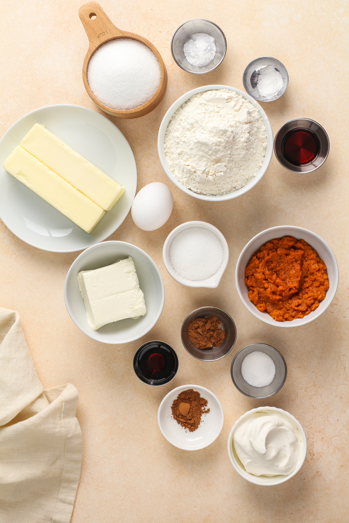 From top left: granulated sugar, baking soda, baking powder, butter, egg, flour, vanilla, cream cheese, additional sugar, pumpkin puree, additional vanilla, pumpkin pie spice, sugar and spices for garnish, whipped cream for garnish.