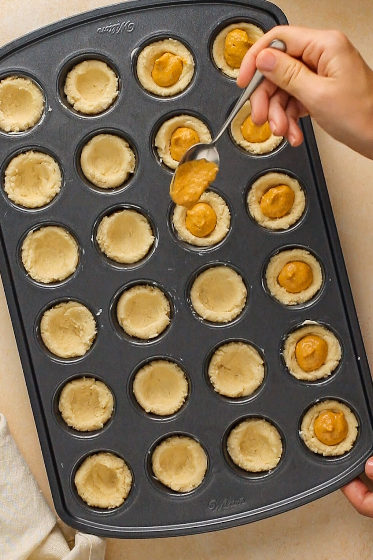 Pie filling being spooned into unbaked cookie cups.