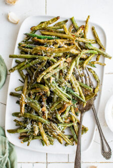 A rectangular white serving platter piled with roasted green beans.