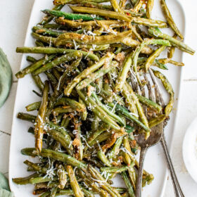 A rectangular white serving platter piled with roasted green beans.