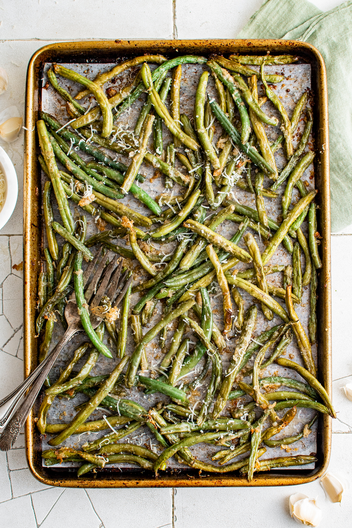 A sheet pan with a sheet of parchment and a layer of roasted green beans on it.