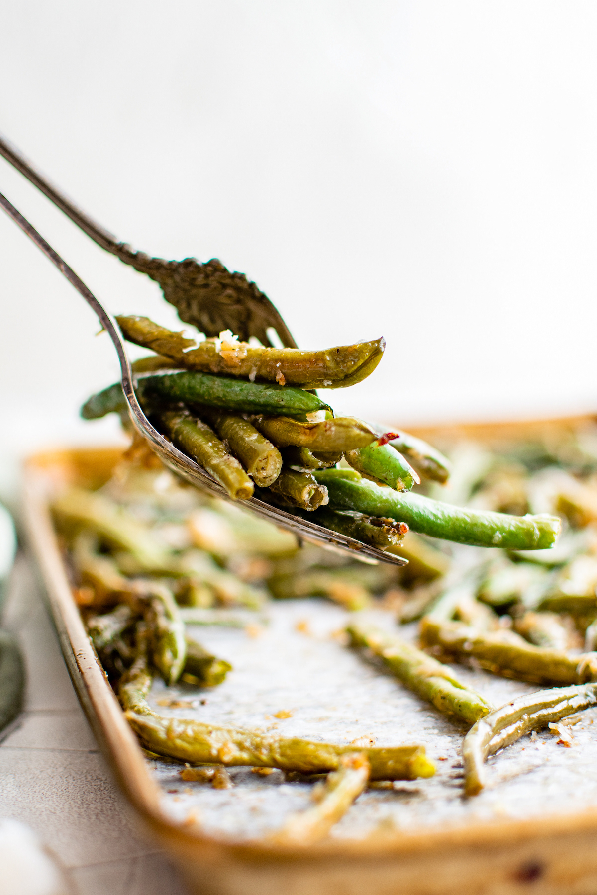 Green beans lifted from a sheet pan with two forks.