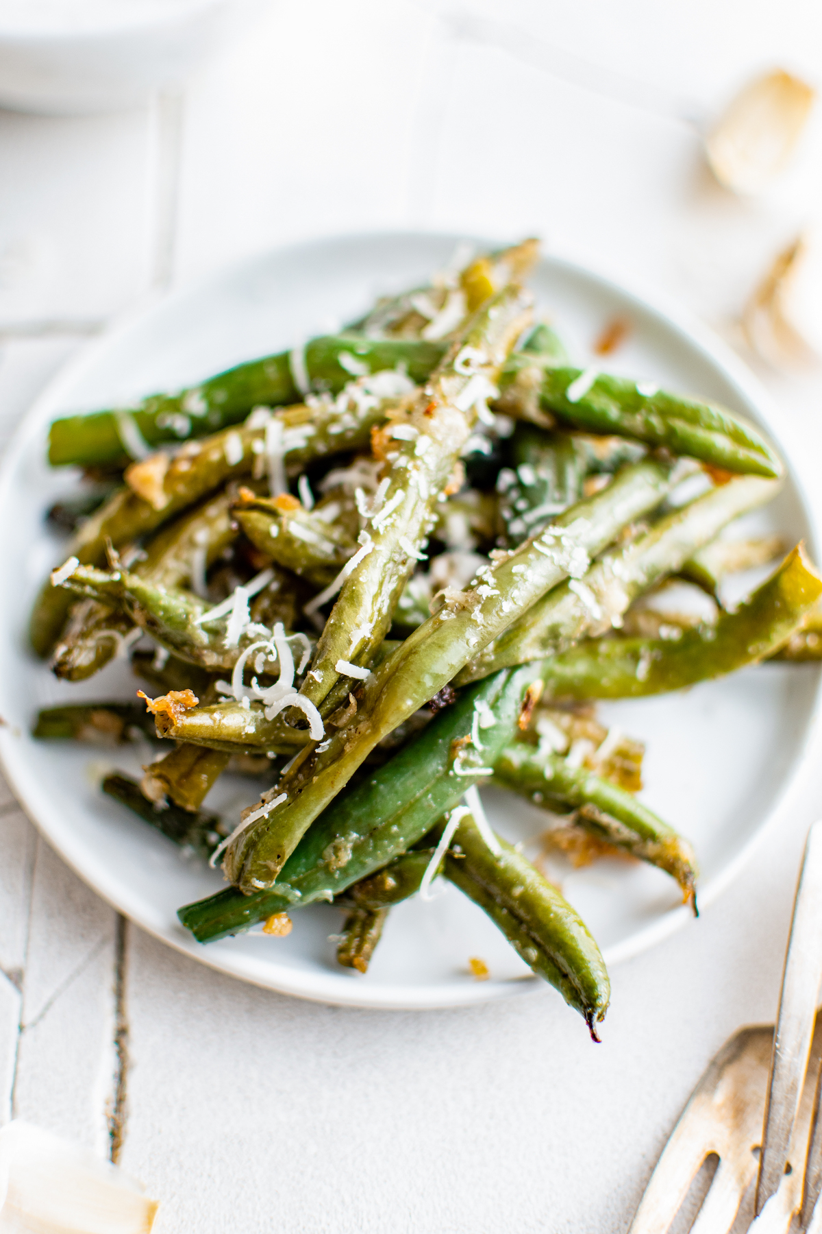A serving of crisp, slightly golden, baked green beans on a small white plate.