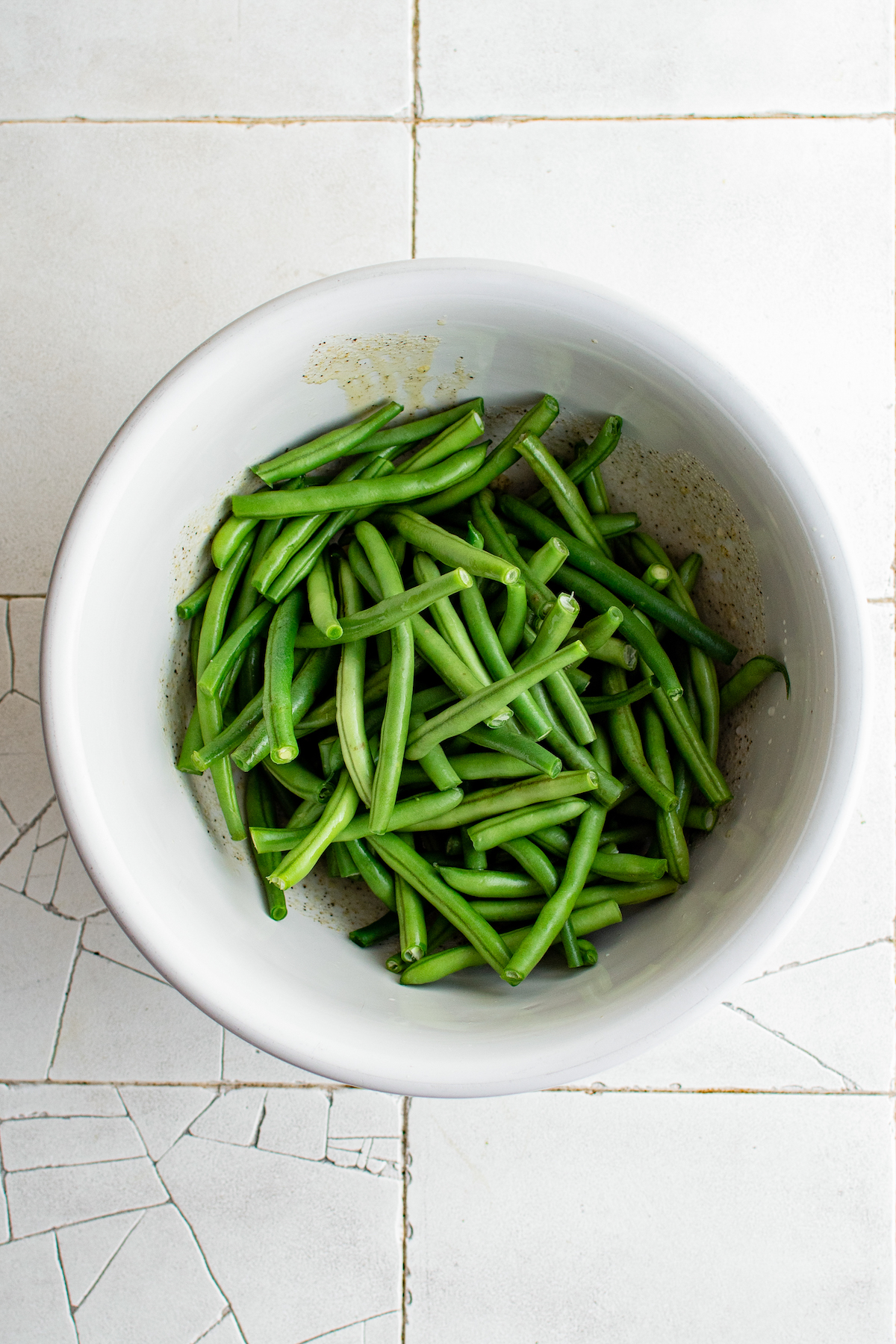 Green beans tossed with oil and seasonings in a mixing bowl.