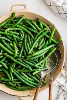 Sauteed green beans in a skillet, with metal serving spoons.