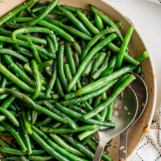 Sauteed green beans in a skillet, with metal serving spoons.