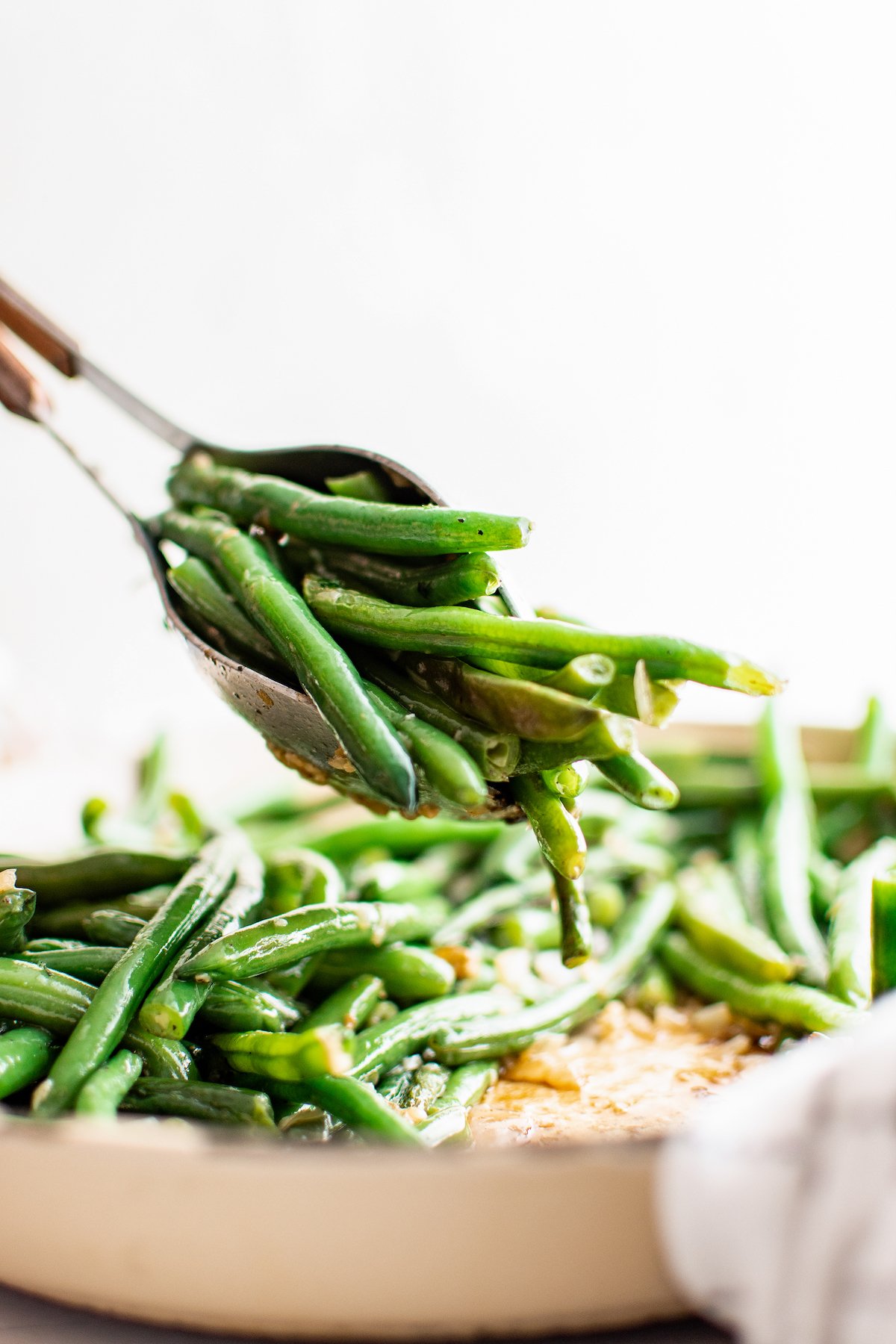 Green beans being lifted out of a pan with two serving spoons.