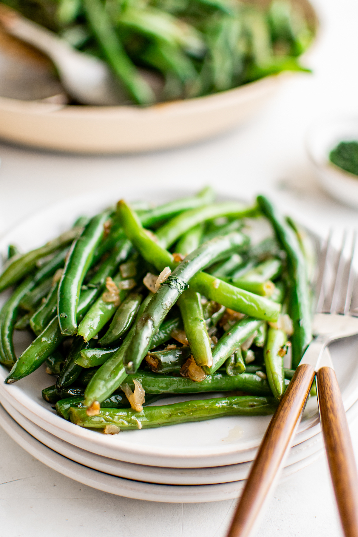 A serving of buttery green beans on a small plate, with a knife and fork.