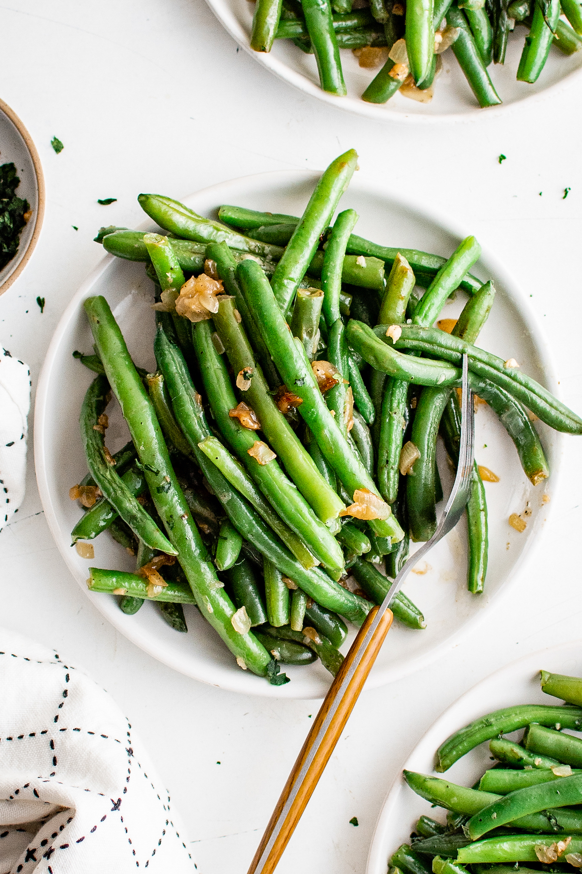 Green beans with garlic on a small plate with a fork. Other small plates of beans are visible in the shot.