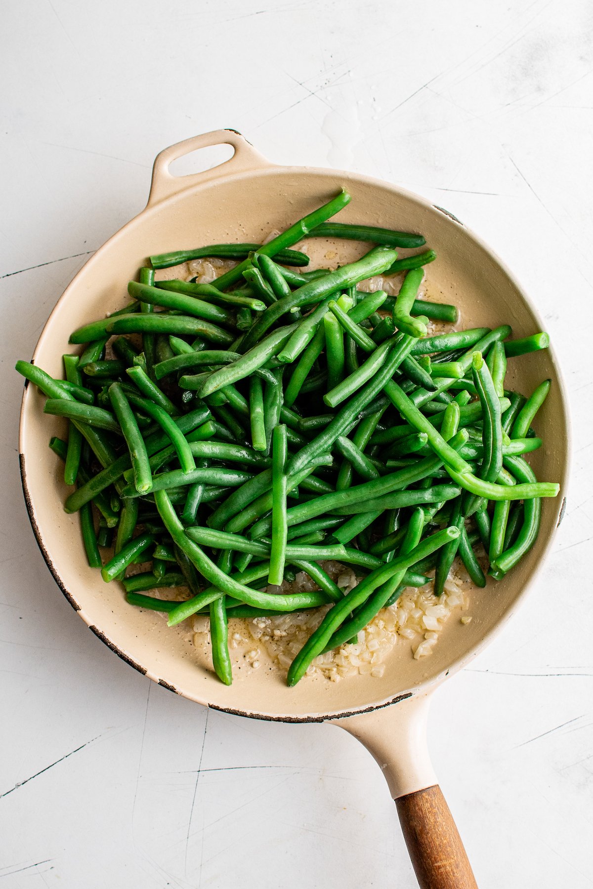 Green beans in a skillet with onions, butter, and other ingredients.