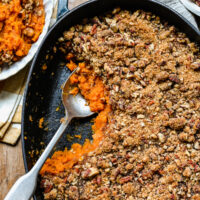 An overhead shot of a sweet potato casserole in a cast-iron baking dish, topped with chopped pecan topping.