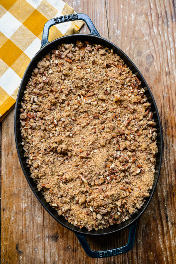 An unbaked casserole in a cast iron dish, topped with chopped nut topping.
