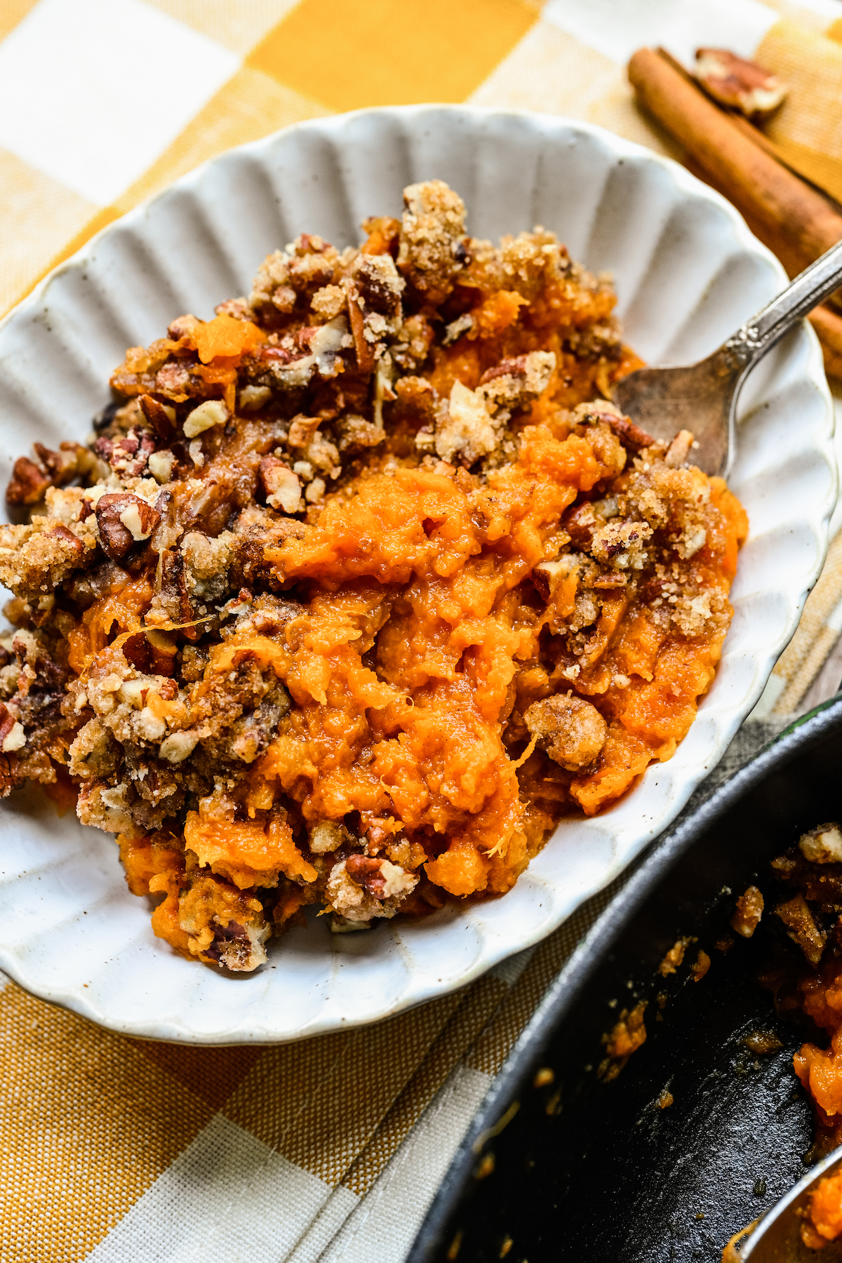 A serving of homemade casserole with sweet potatoes and pecans, placed on a white plate with fluted edges.