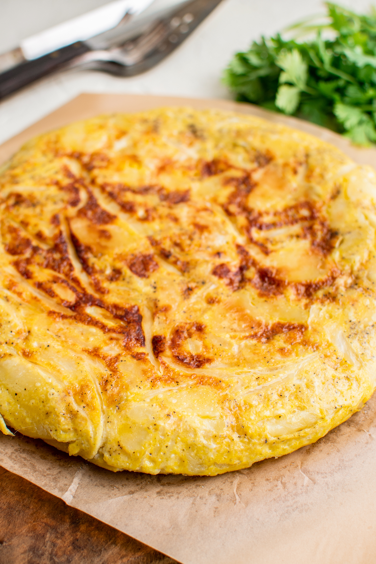A close up of a whole tortilla española on a cutting board, with parsley in the background