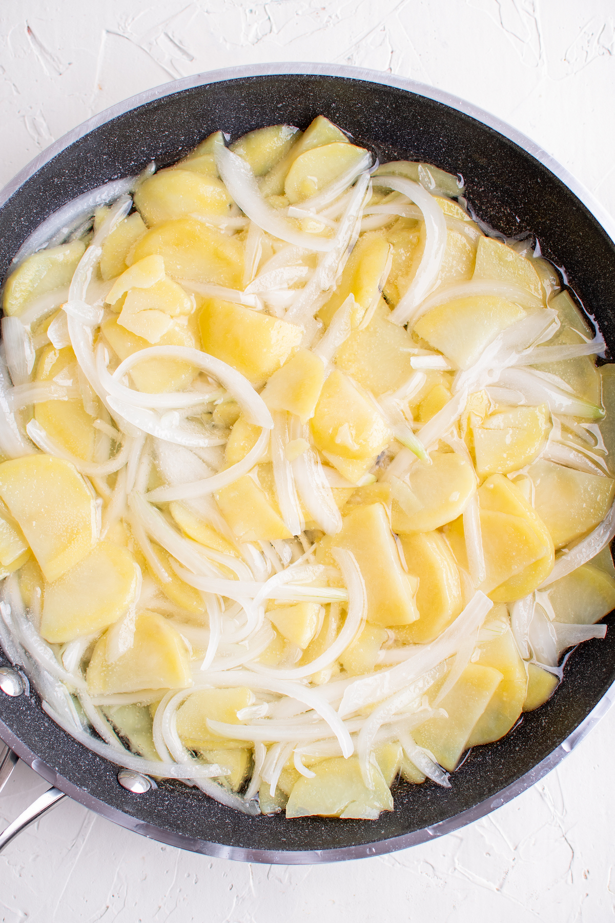 A skillet filled with half-moon slices of potatoes, and slices of onions in oil