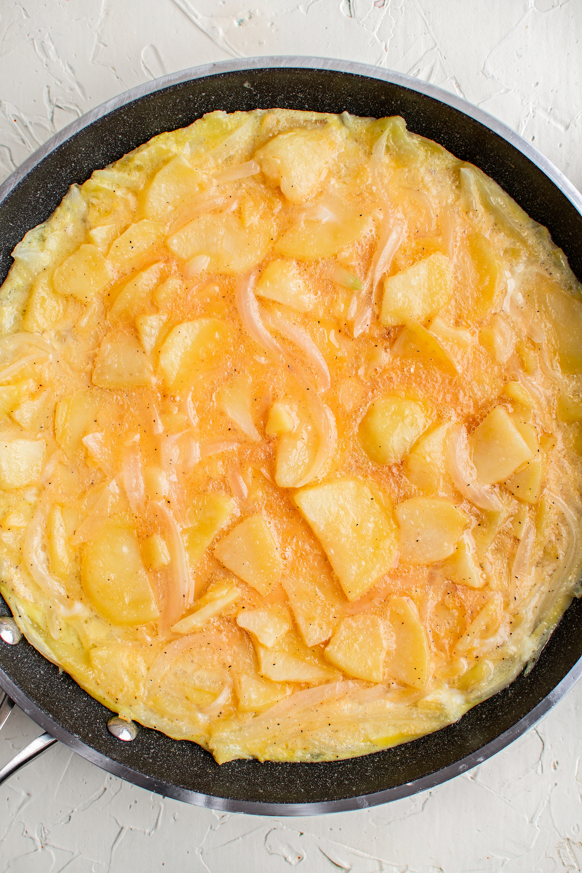 A skillet with uncooked beaten eggs, potatoes, and onions in it
