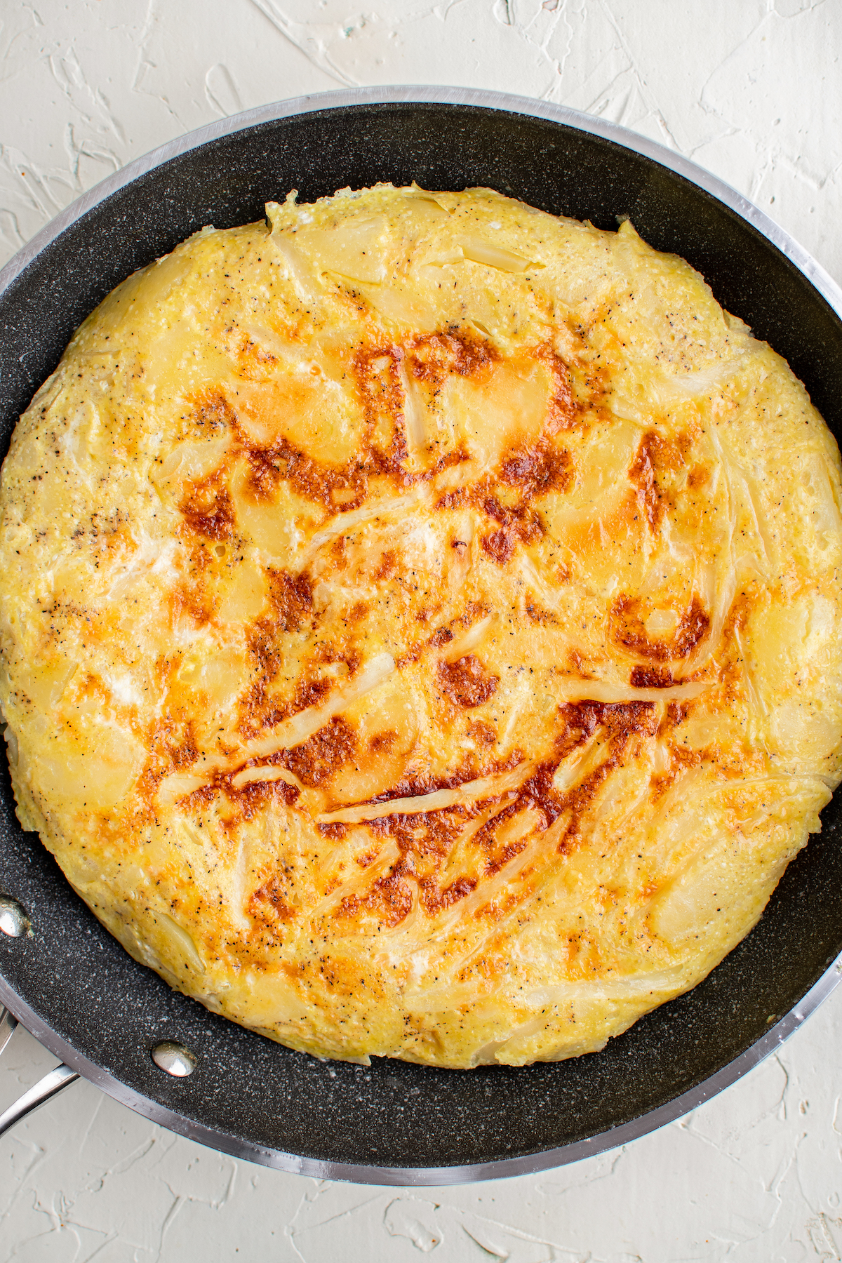A tortilla española that has been flipped, in a skillet, with a golden exterior