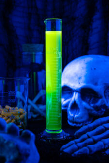 A glowing halloween shot in a test tube with a skeleton in the back ground.
