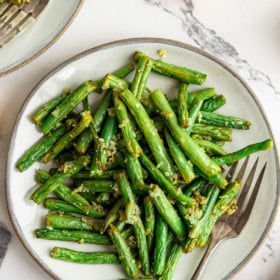 A plate of cooked green beans with a fork.