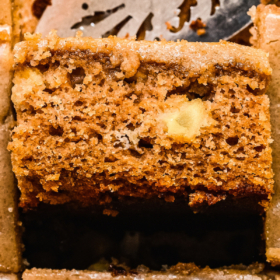 A slice of apple cake flipped on it's side in a pan of cake.