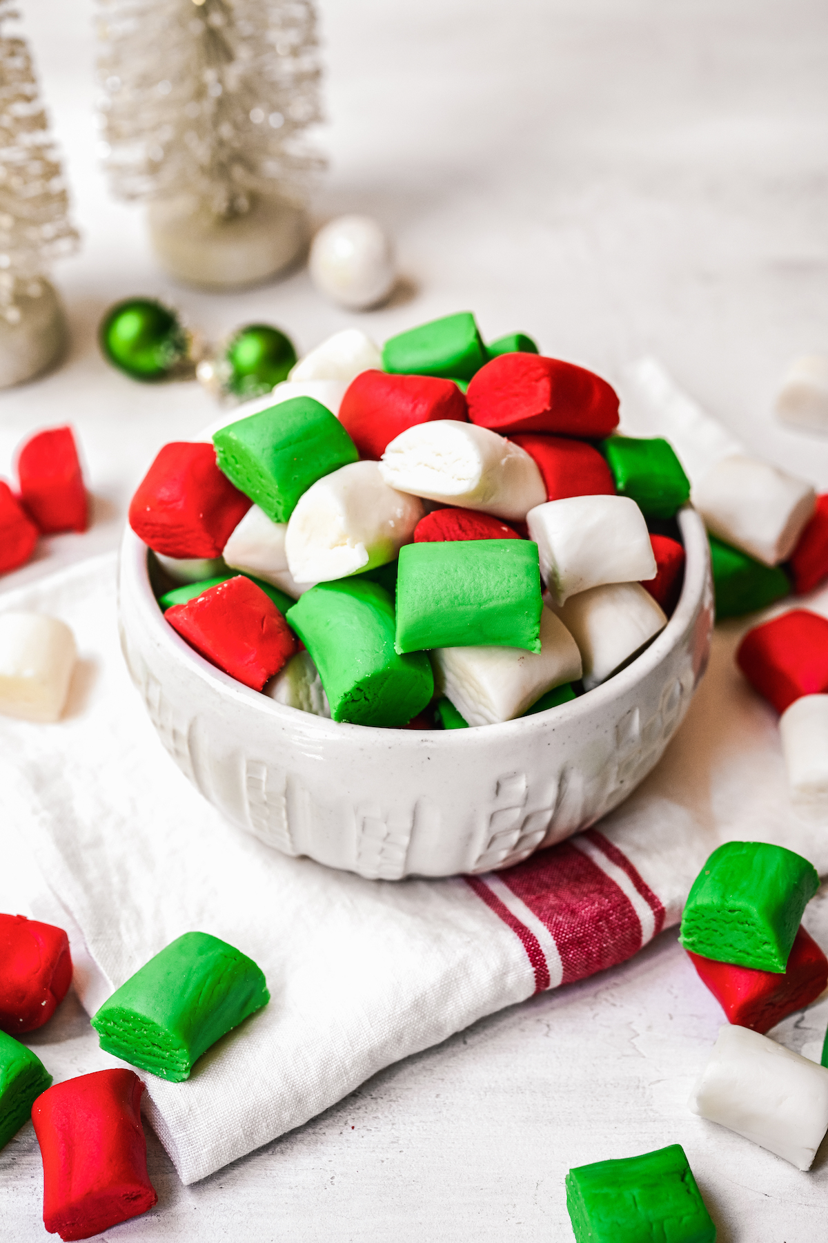 Red, white, and green mints in a small candy dish. More mints are scattered on the table.