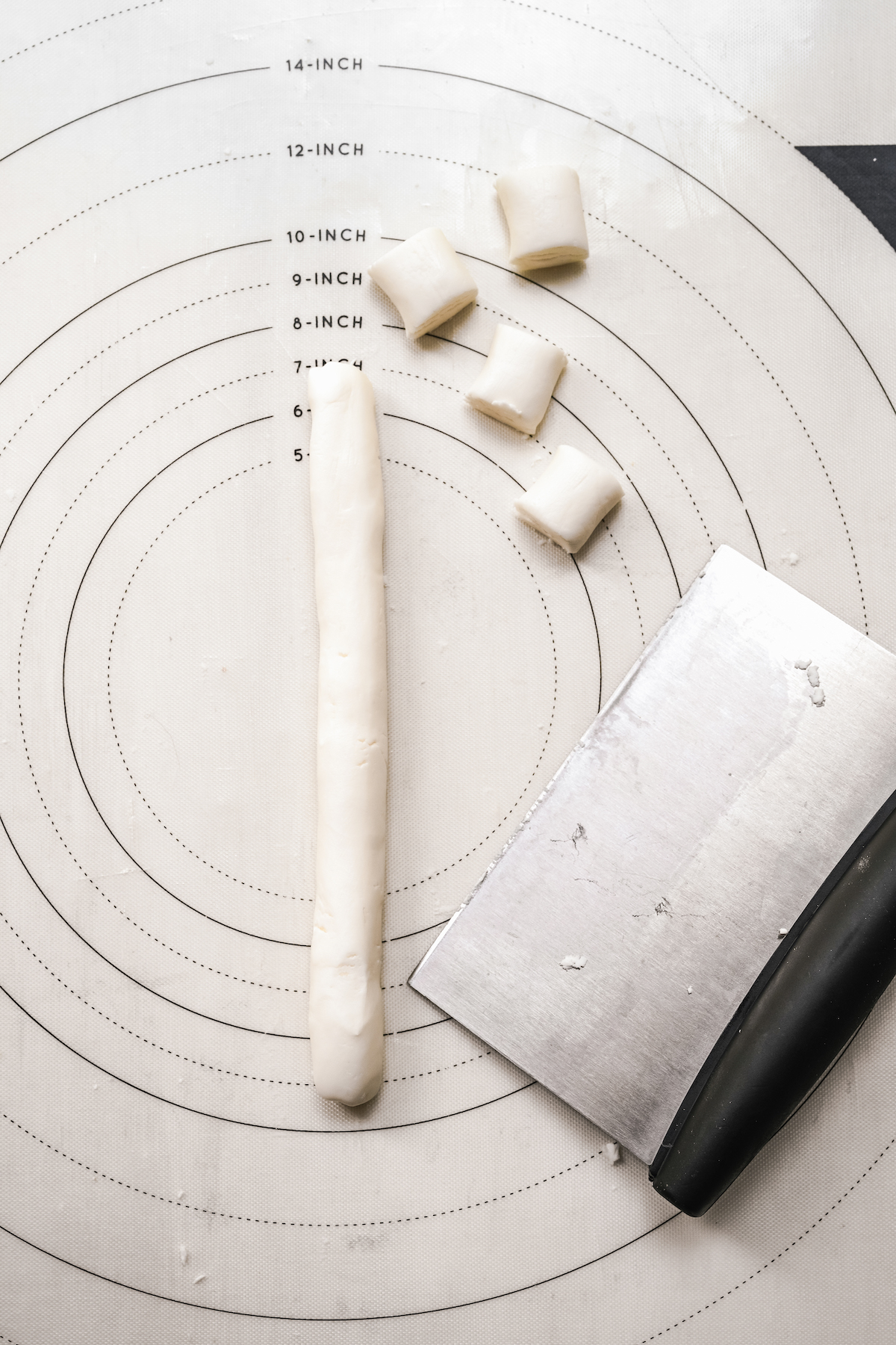 A rope of mint dough, with several small pieces cut off. A bench scraper is nearby on the work surface.