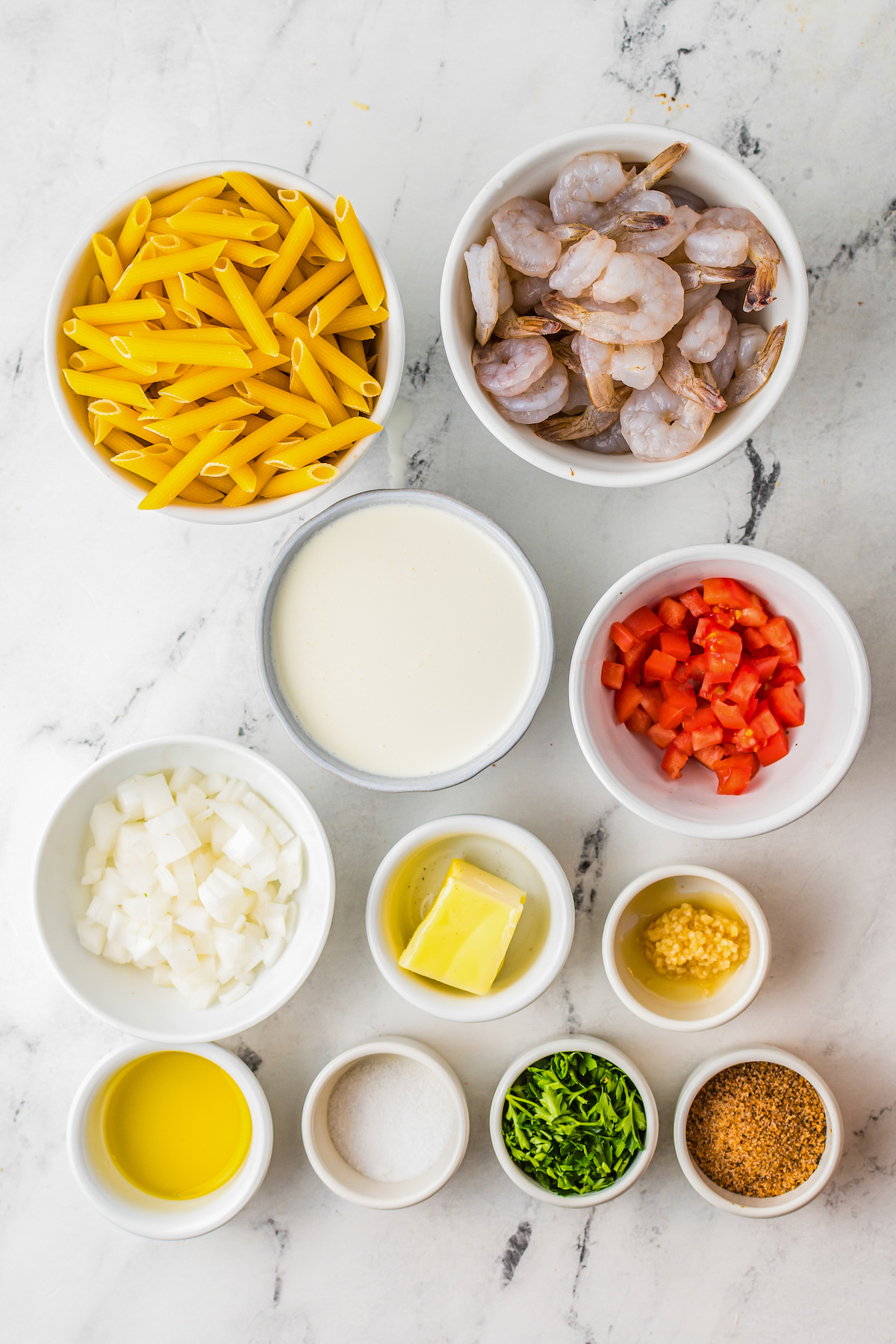 From top left: Dry penne pasta, raw shrimp, heavy cream, diced tomato, diced onion, butter, garlic, olive oil, salt, parsley, cajun seasoning.