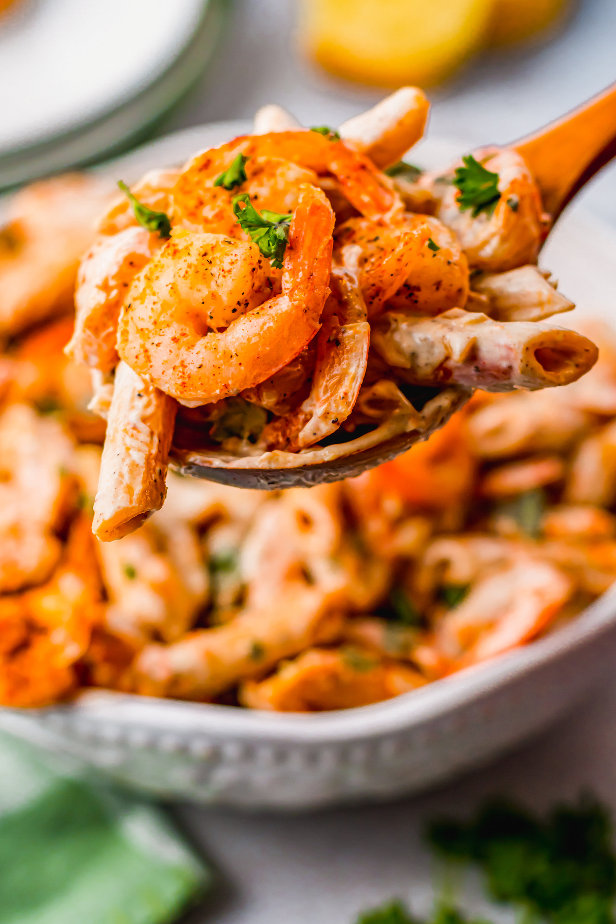 Lifting shrimp and pasta toward the camera with a wooden spoon.