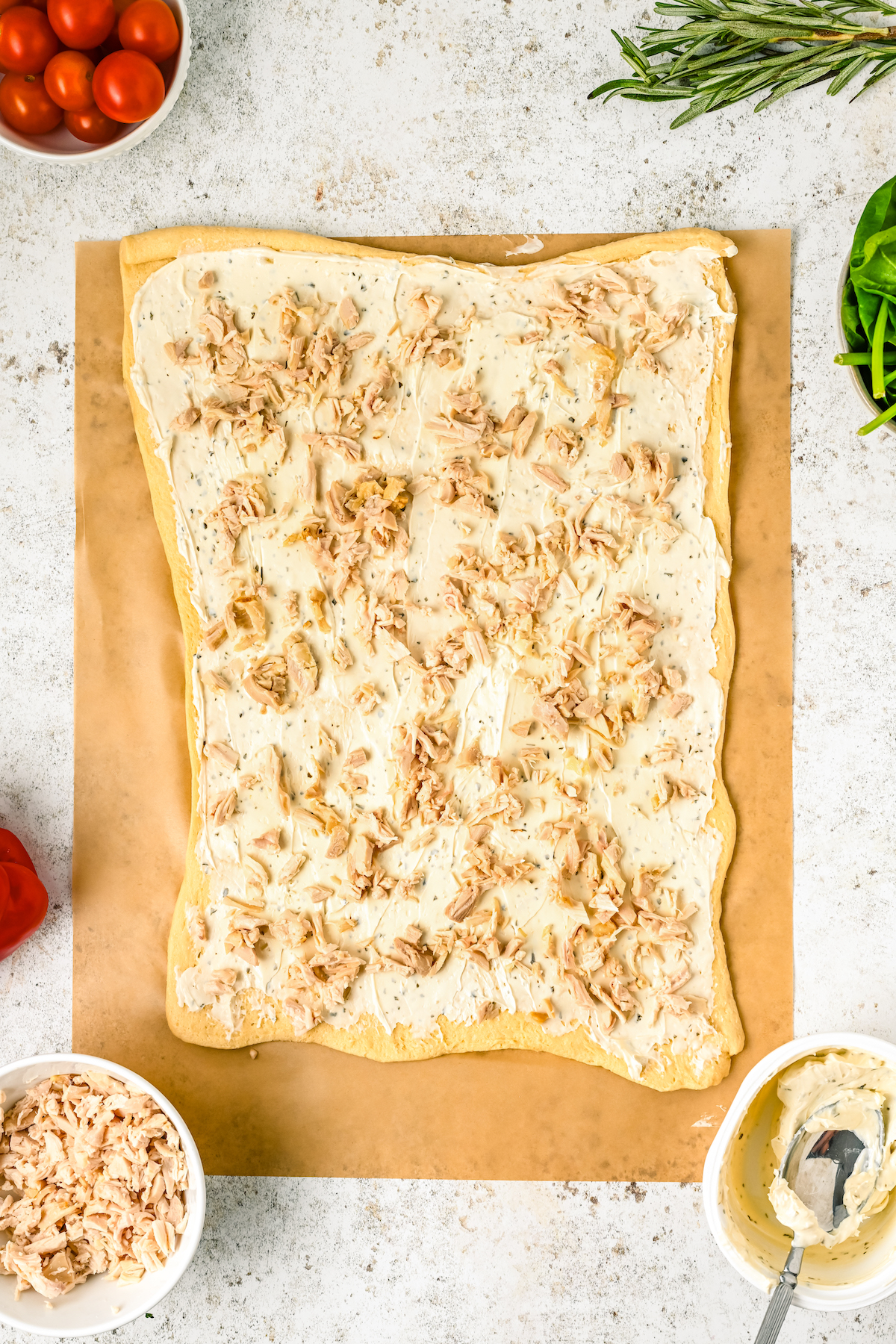 A rectangle of crescent roll dough, topped with cream cheese and shredded chicken.