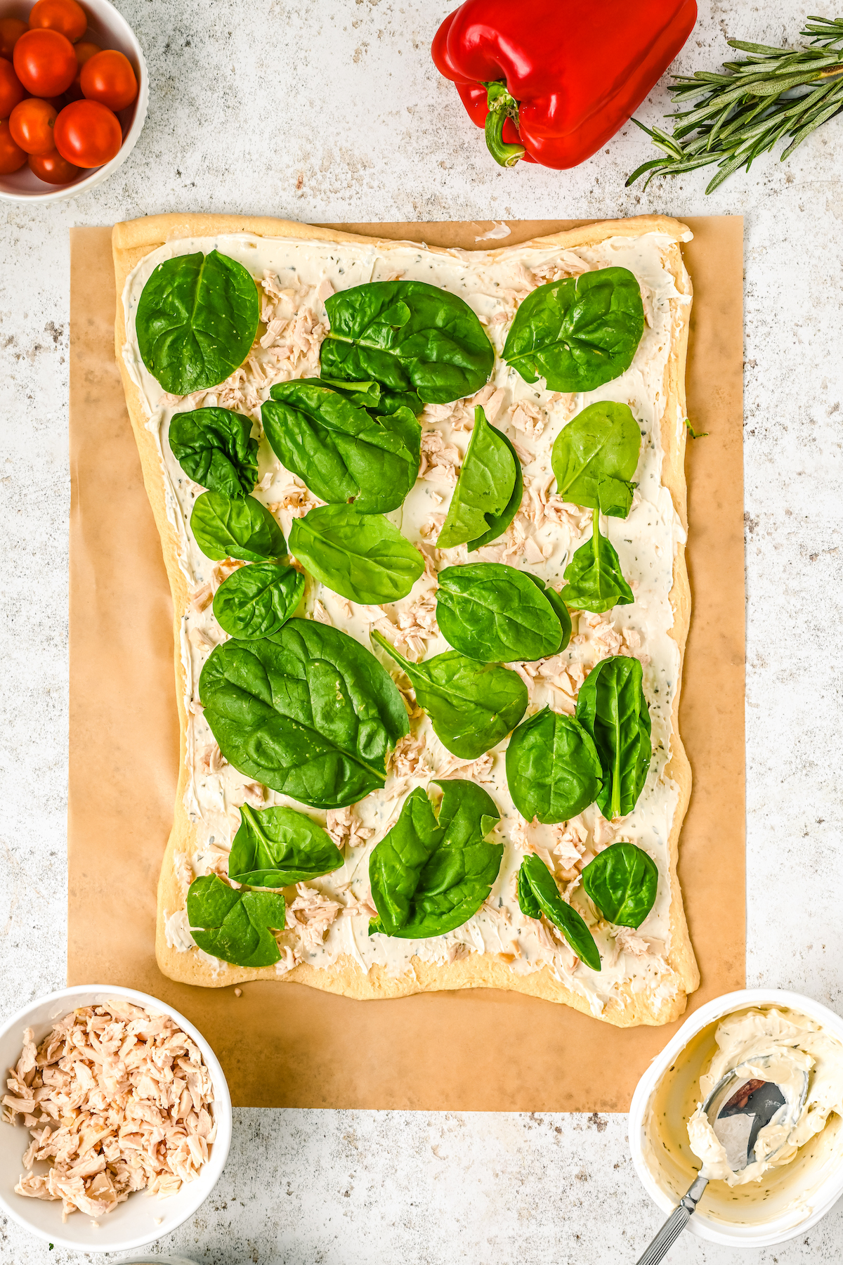 Spinach leaves laid over chicken and cream cheese on raw crescent dough.