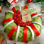 A cake covered in green icing, decorated with red and white ribbons and other Christmas items.