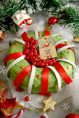 A cake covered in green icing, decorated with red and white ribbons and other Christmas items.