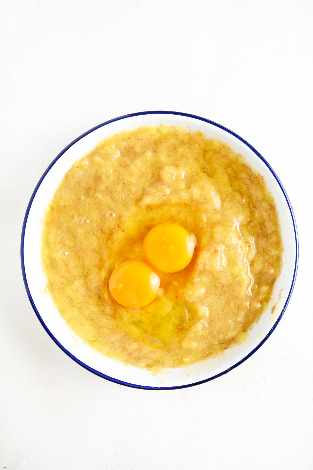 A bowl of banana cake batter with eggs being added.